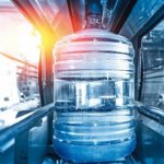 Plastic_bottle_or_gallon_of_purified_drinking_water_inside_automated_conveyor_production_line._Water_factory,_blue_toned_with_sunlight_flare.